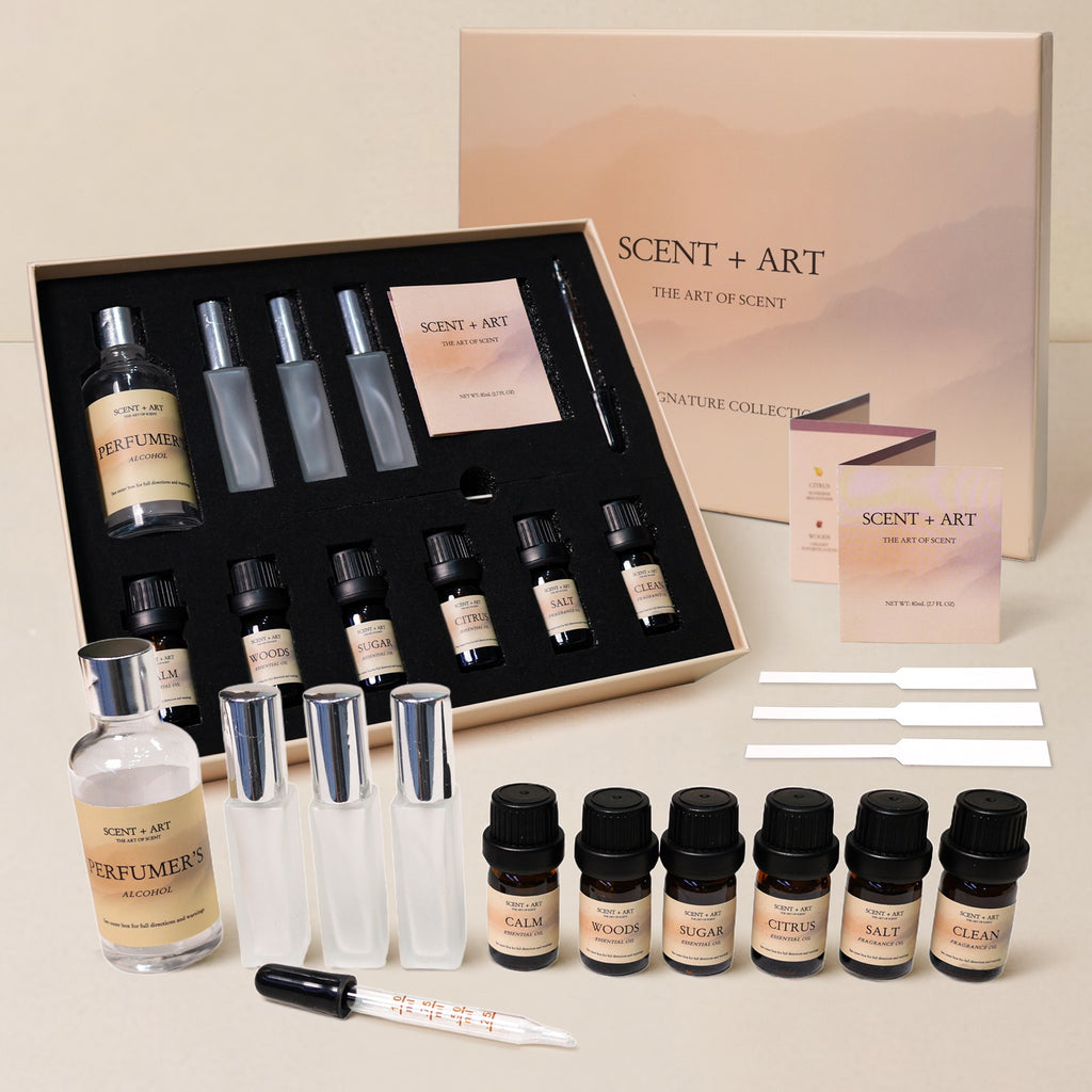 perfume making kit with open luxury box showing six perfume oils, three empty spray bottles, perfumer's alcohol, dropper, and instruction materials on neutral background